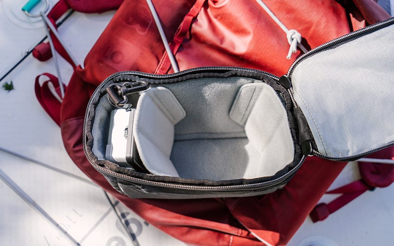 An X-Small Camera Cube V2 sits open on a red bag.