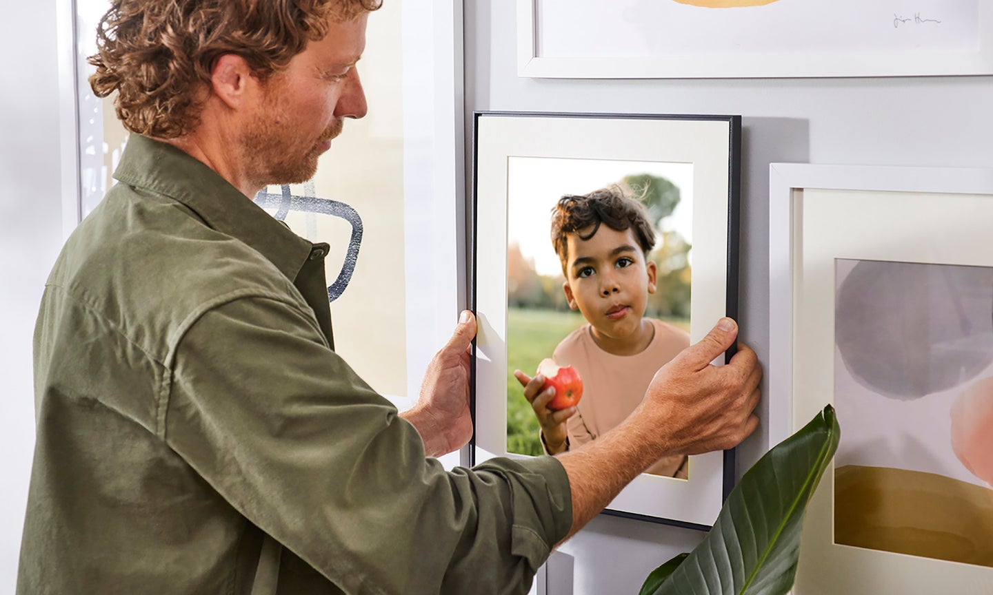 A man hangs the Aura Walden digital photo frame on the wall.